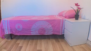 A single bed with a pink patterned bedspread, a white nightstand, and a potted plant with flowers. - Quiet single room (Madrid)