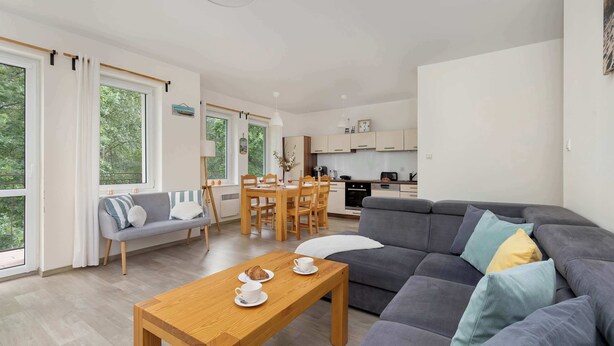 A modern living room with a sofa, a dining table, and a kitchen in the background.