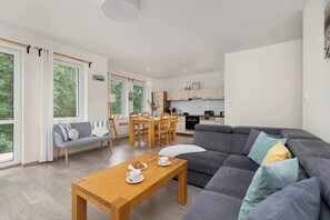 A modern living room with a sofa, a dining table, and a kitchen in the background. - Spacious Apartment with Balcony | 100 m to the Beach (Międzyzdroje)