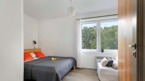A bedroom with a bed, a bedside table, a chair, and a window with a view of trees.