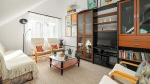 Una sala de estar con una mesa de centro de vidrio, dos sillones, un sofá, un televisor, un mueble con puertas de vidrio y una estantería.
