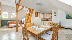 Un comedor con una mesa de madera dispuesta para cuatro personas, un sofá, una escalera y una cocina al fondo.