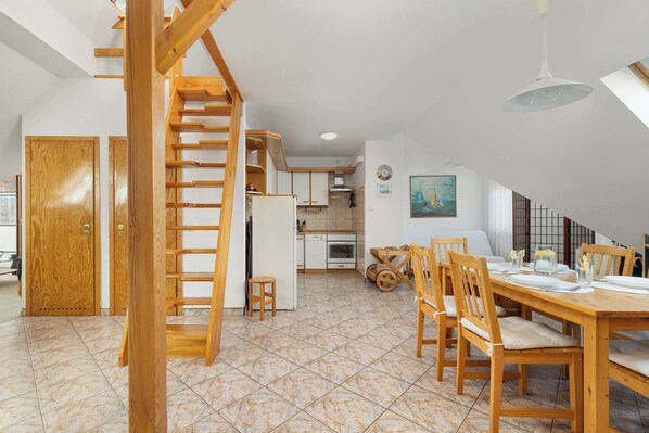 Une cuisine spacieuse équipée d’appareils modernes, un coin repas avec des meubles en bois et un escalier menant à l’étage supérieur.