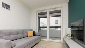 Un soggiorno moderno con un divano grigio, un tappeto soffice, una TV su un mobile bianco e una porta vetrata scorrevole che dà su un balcone.