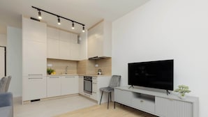 Una cucina moderna con elettrodomestici integrati, una zona pranzo con un divano grigio e una TV su un mobile bianco.