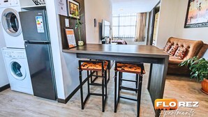 A kitchen with a built-in washing machine, a bar stool, and a brown leather sofa. - H1 - 14th Floor Modern Studio with Stunning City Views, Wi-Fi & Washer/Dryer (La Paz)