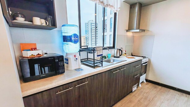 A modern kitchen with a built-in microwave, a water dispenser, a kettle, and a gas stove. - H1 - 14th Floor Modern Studio with Stunning City Views, Wi-Fi & Washer/Dryer (La Paz)