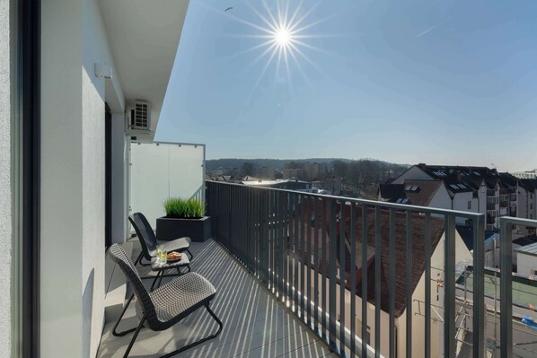 A balcony with a view of a cityscape, a table with chairs, and a potted plant.