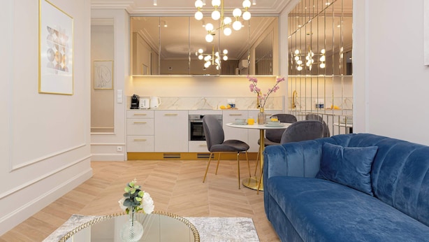 A modern living room with a blue sofa, a glass coffee table, and a dining area with a round table and chairs.