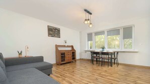 Una sala de estar con un sofá gris, una mesa de comedor de madera con sillas, un mueble aparador y un candelabro en el techo.