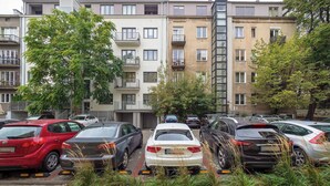 Un estacionamiento con varios coches aparcados frente a un edificio residencial de varios pisos con balcones.
