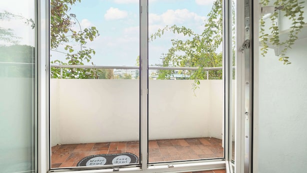 Un balcón con puerta de vidrio, baranda de metal y piso de baldosas.