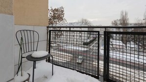 A balcony with a metal chair and a small table covered in snow, overlooking a parking area with snow on the ground. - Spacious Apartment | 2 Bedrooms | Workspace (Warszawa)