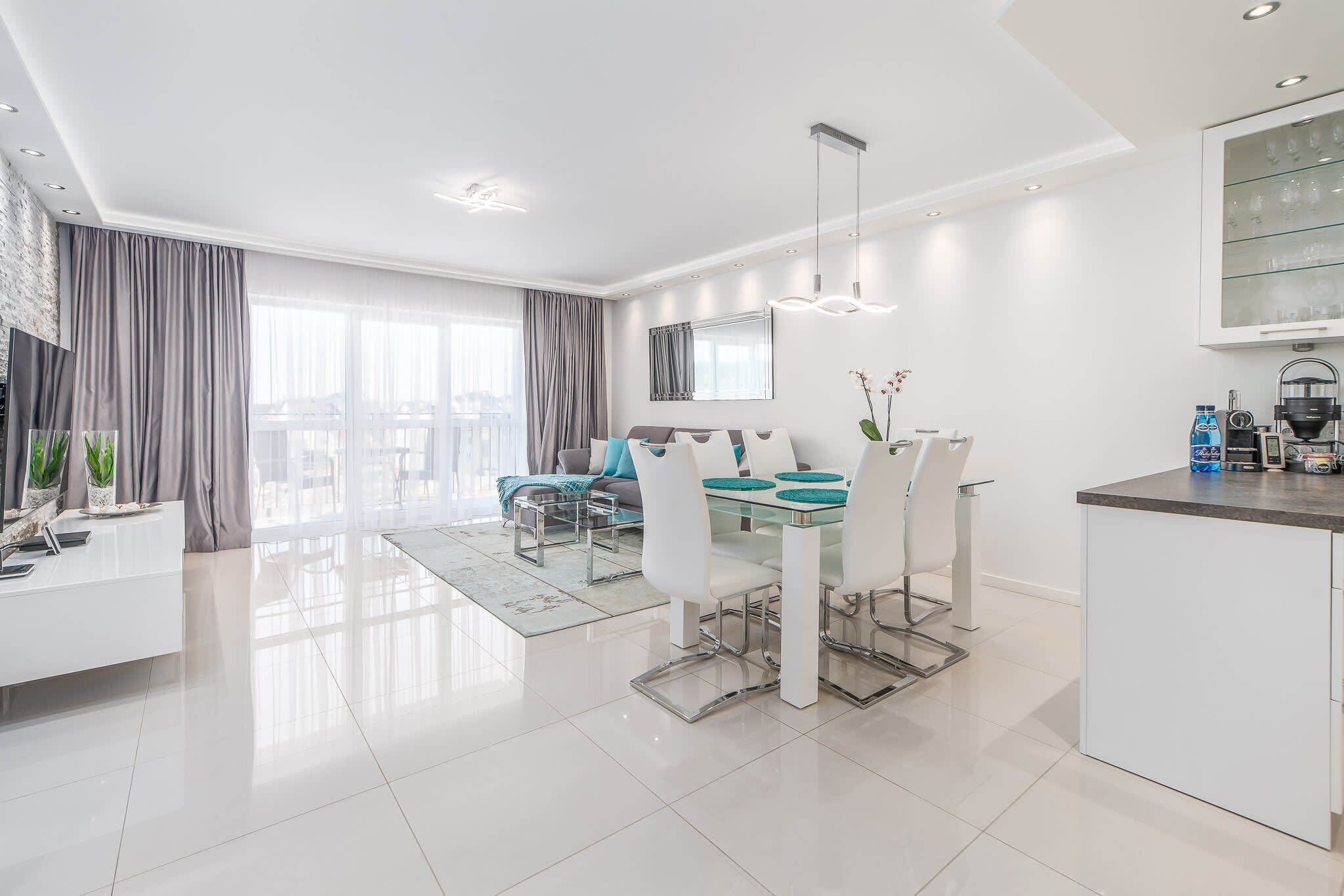 A modern living room with a dining area, a kitchen, and a large window.