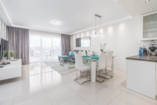 A modern living room with a dining area, a kitchen, and a large window.