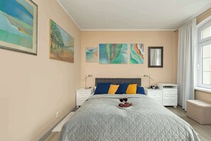 Une chambre à coucher avec un lit, des tables de chevet, des œuvres d’art et une fenêtre.
