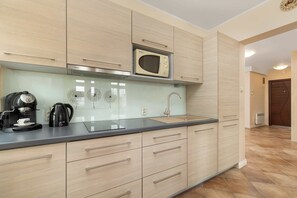 Una cocina con armarios de madera clara, un microondas, una cafetera y un lavabo.