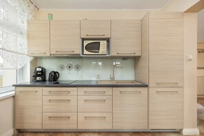 Une cuisine moderne avec des meubles en bois clair, un four à micro-ondes encastré, une machine à café et un pare-feu en verre.