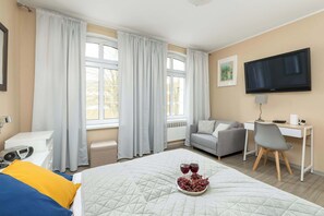 Una habitación de hotel con cama, escritorio, silla, televisión y ventana con cortinas.
