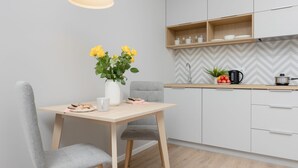 A modern kitchen with a wooden table and grey upholstered chairs, a vase of yellow flowers, and a herringbone-patterned backsplash. - Modern Studio | Private Parking | Close to Metro (Warszawa)