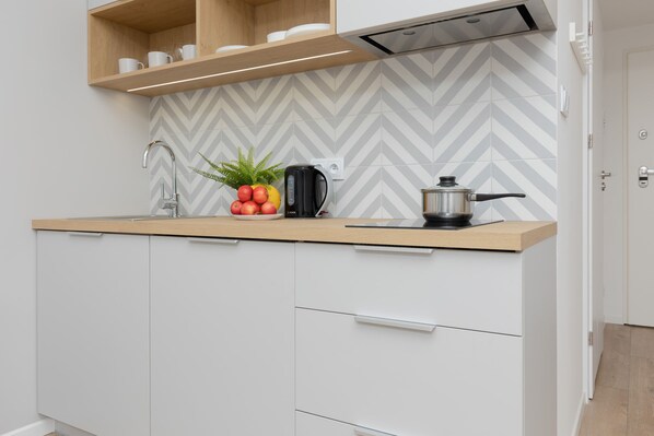 A modern kitchen with white cabinets, a wooden countertop, a kettle, a pot, and a fruit bowl with apples and a plant.