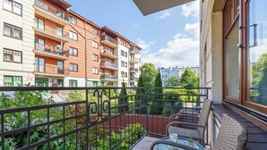 Ein Balkon mit Tisch und Stühlen, umgeben von einem Metallgeländer, mit Blick auf einen Garten und benachbarte Gebäude.