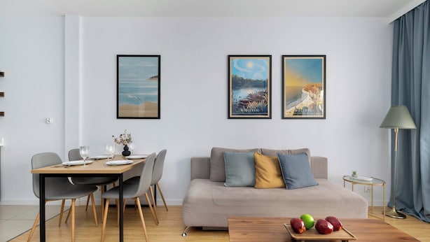 Ein modernes Wohnzimmer mit Esstisch, grauem Sofa und Kunstwerk an der Wand.