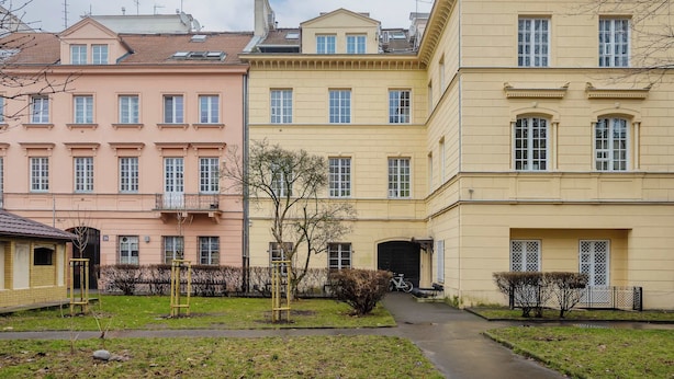 Eine Reihe mehrstöckiger Gebäude mit einheitlichen Fenstern und Balkonen, ein gepflasterter Weg und eine kleine Rasenfläche mit einem Fahrrad.