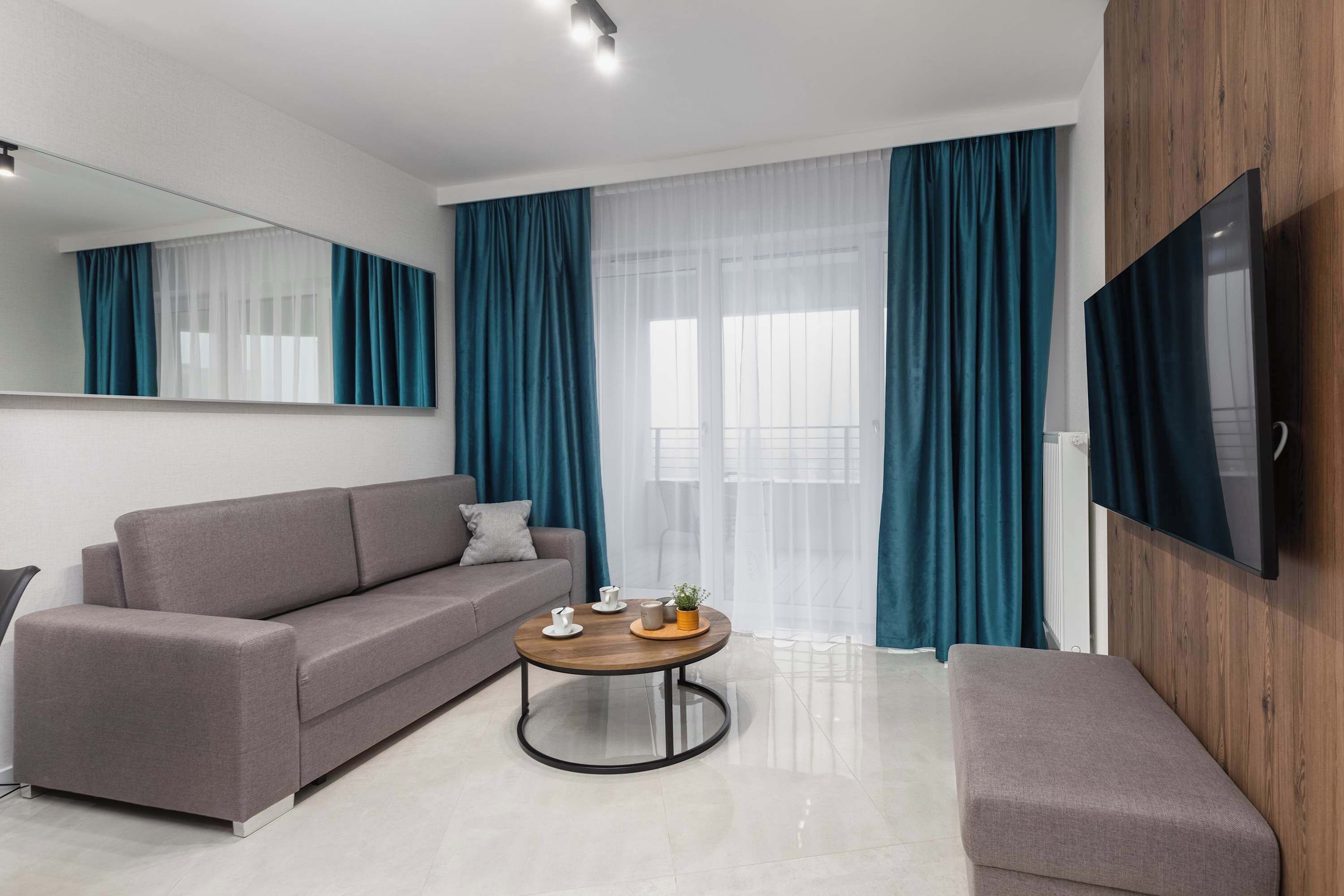 A modern living room with a grey sofa, a round coffee table, and a TV mounted on the wall.