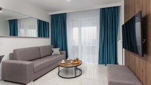 Un salon moderne avec un canapé gris, une table basse ronde et un téléviseur fixé au mur.