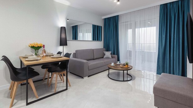 Un salon moderne avec un canapé gris, une table basse ronde et un coin repas comprenant une table en bois et des chaises noires.