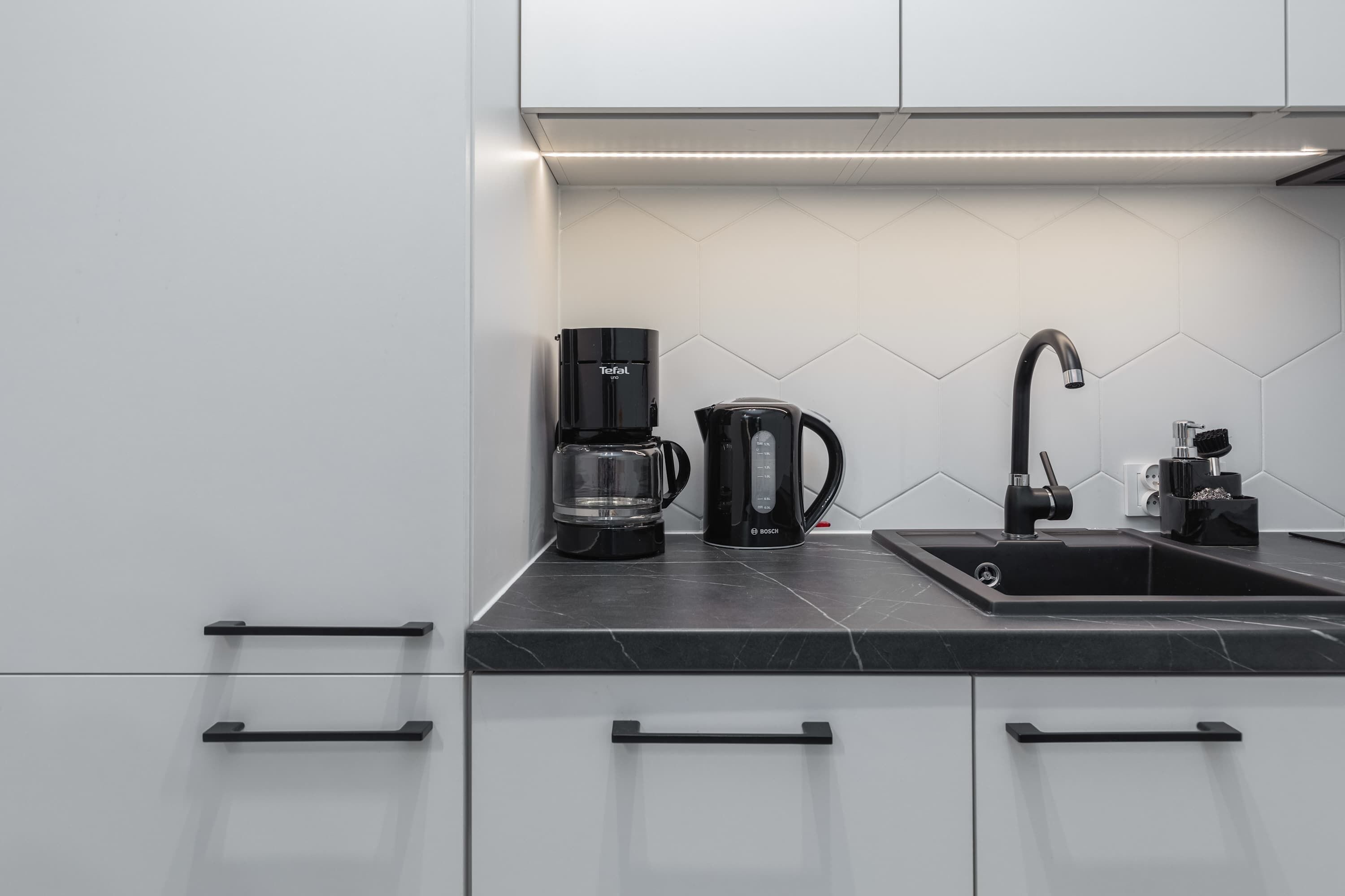 A modern kitchen with a black Bosch coffee maker, a glass carafe, and a black sink.