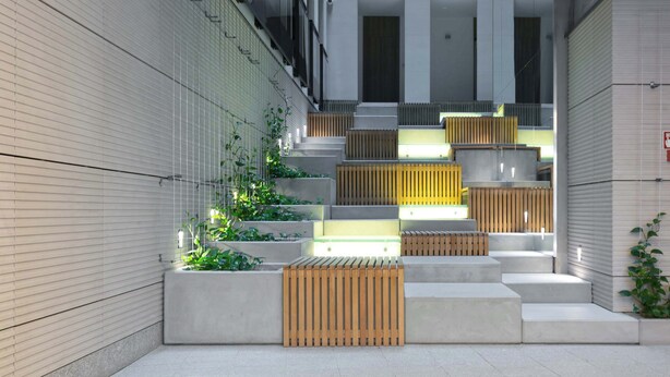 A modern building with a series of steps leading up to a landing area with planters and lighting.