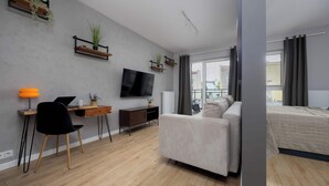 A modern bedroom with a bed, a desk with a laptop, a chair, and a TV on the wall.