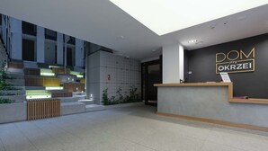 A modern reception area with a reception desk, a staircase, and a sign that reads "DOM przy OKRZEI".