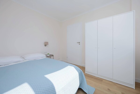 A bedroom with a bed, a wardrobe, a nightstand, and a wall-mounted light.