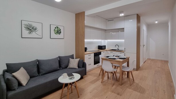 A modern apartment with a grey sofa, a small round table, and a dining area with a wooden table and chairs. - Modern Studio in the Center | Balcony | Close to Market Square (Nowy Sącz)