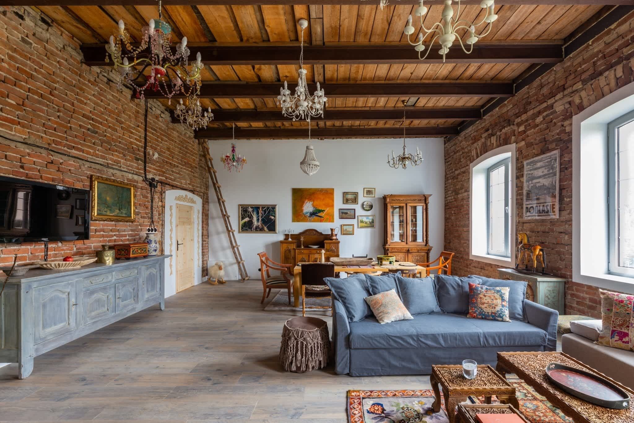 A rustic interior with exposed brick walls, wooden beams, a dining area, and a blue sofa.