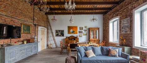 A rustic interior with exposed brick walls, wooden beams, a dining area, and a blue sofa.
