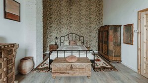 Une chambre à coucher avec un lit, une commode, un grand vase et un papier peint à motifs.