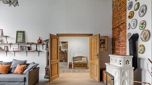 Un salon chaleureux avec un canapé, des portes ouvertes donnant sur une autre pièce, une cheminée et un mur décoré d’assiettes.
