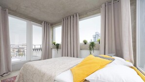 A bedroom with a large bed, a view of the city, and a balcony with plants. - Spacious Apartment for 8 Persons | Air Conditioning (Warszawa)