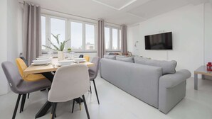 A modern living room with a grey sofa, a dining table set for four, and a flat-screen TV mounted on the wall. - Spacious Apartment for 8 Persons | Air Conditioning (Warszawa)