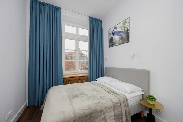 A bedroom with a bed, a window with curtains, a small table with a plant, and a painting on the wall. - Spacious Apartment with a View of the Castle | Old Town (Warszawa)