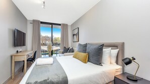 A modern hotel room with a large bed, a desk, a TV, and a view of the outdoors.