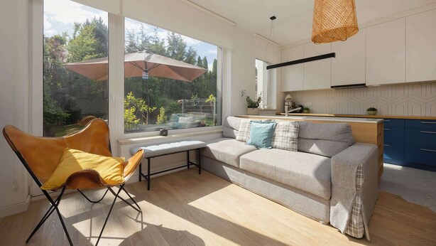 A modern living room with a sofa, a chair, and a bench by a large window overlooking a garden.