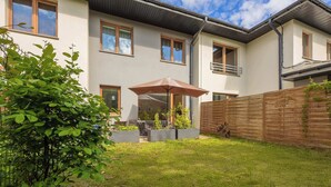 A modern two-story house with a well-maintained garden, a patio with outdoor furniture, and a wooden fence.
