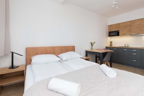 Une chambre d’hôtel comprenant un lit, un bureau, une chaise, une table de chevet et un coin cuisine avec des placards et un four à micro-ondes.