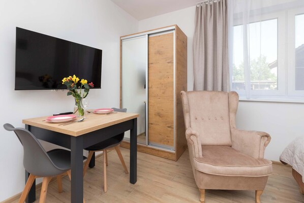 Una habitación con una mesa de comedor de madera, un televisor montado en la pared, un armario corredero y una ventana con cortinas.