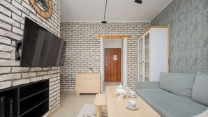 A living room with a stone wall, a flat-screen TV, a wooden table with a teapot, and a grey sofa.